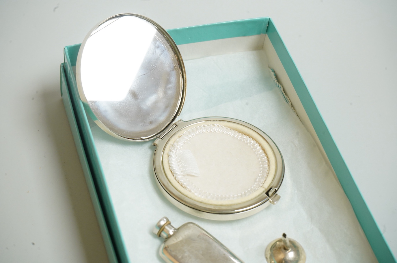 A small modern Tiffany & Co sterling scent flask, 44mm, together with a Tiffany & Co sterling compact, diameter 64mm and a small unmarked white metal funnel, with an associated Tiffany & Co box.